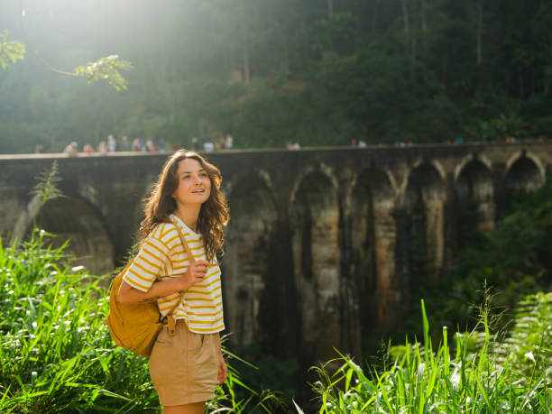 Cheerful woman standing near nine arch bridge in Sri Lanka at sunset